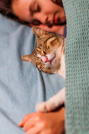 boy falls asleep and hugs his cat, who sleeps with him under the covers. children and pets. the cat sleeps with the baby. the child is getting ready for bed.の写真素材