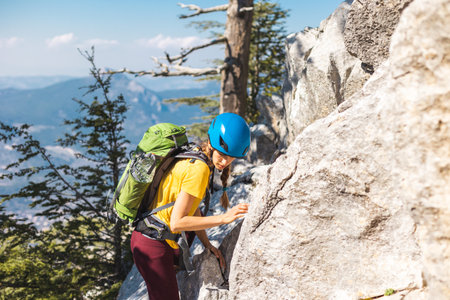 The girl is climbing the rock. Woman climber with a backpack and a helmet in the mountains. adventure and mountaineering concept. hiking with a backpack in the mountains. mountains of Turkey.の写真素材