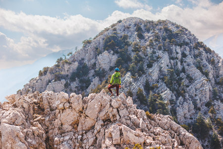 climber with a backpack and a helmet stands on top of the mountain. Girl climber in the mountains. adventure and mountaineering concept. hiking with a backpack in the mountains.の写真素材