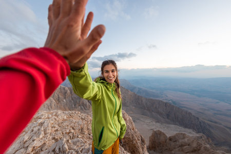 A woman with a backpack climbed to the top of the mountain and gives a high five, hiking in the mountains, success in achieving the goalの写真素材