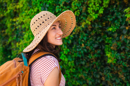 portrait of a young girl in a hat and with a backpack on the background of a green wall. summer...