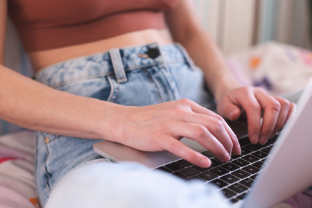 A girl works from home, female hands on a laptop keyboard close-up, a woman sits on a sofa with a laptopの写真素材