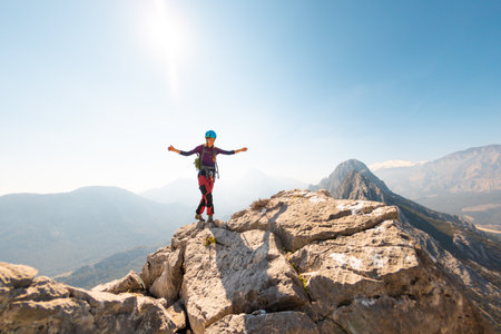young girl climber in a helmet and with a backpack stands on top of a mountain. mountain climbing and hiking.の写真素材