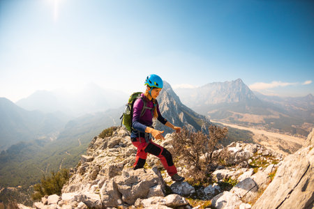 young girl climber in a helmet and with a backpack walks along a mountain range against the backdrop of mountains and climbing and hiking in the mountains.の写真素材