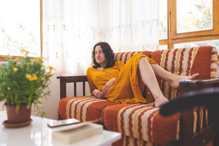 A girl in a yellow dress lies on the sofa, a woman is resting at home, home comfortの写真素材