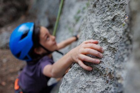 rock climber's hand close-up. child rock climber in a blue protective helmet overcomes the route in the mountains. children's sports in nature. active time in nature.の写真素材