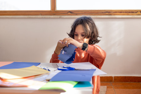 The child makes a snowflake out of colored paper. the boy cuts a snowflake out of blue paper with scissors. children's creativity.の写真素材