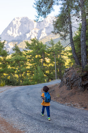 a child with a backpack goes along a mountain road. children's trip. weekend with kids.の写真素材