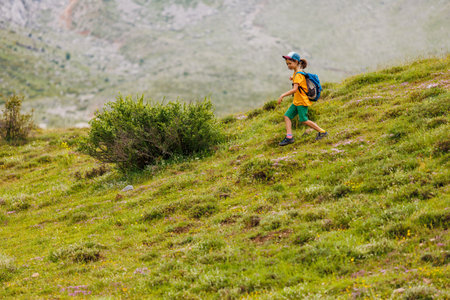 children's trip. child traveler with a backpack resting outdoors with rocky mountains in the background. Concept of summer vacation and hiking lifestyleの写真素材