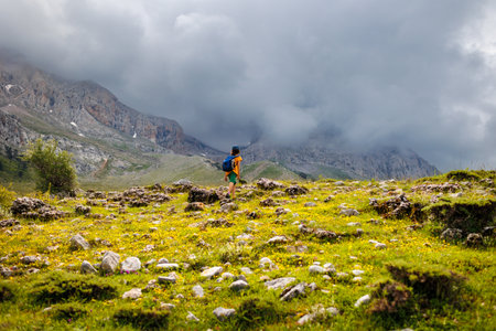 little boy with a backpack in the picturesque mountains. Traveler man with backpack, hiking, travel, lifestyle concept, mountains in the background, summer vacation, outdoor aerial view.の写真素材