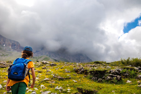 boy with a backpack on a hike against the backdrop of the mountains. child traveler with backpack, hiking, travel, lifestyle concept, mountains in the background, kids summer vacation.の写真素材