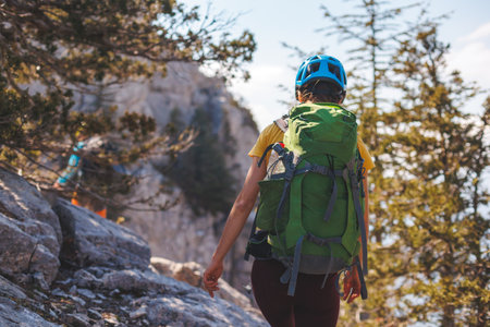 climber with a backpack and a helmet goes along a mountain path in the mountains. Girl climber in the mountains. adventure and mountaineering concept. hiking with a backpack in the mountains.の写真素材