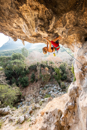 A young rock climber on an overhanging cliff. The climber climbs the rock. The girl is engaged in sports climbing. Sports in nature.の写真素材