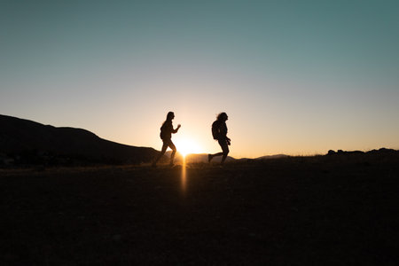 Running people over rough terrain. two girls train outdoors in a beautiful mountain landscape at sunset. silhouette of two girls during a hike in the mountains.の写真素材