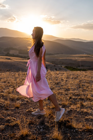 girl walks against the backdrop of the mountains. a young girl in a pink dress enjoys a walk in the mountains.の写真素材