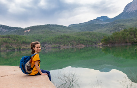 A child with a backpack looks at a beautiful mountain lake. Relaxed, peaceful, thoughtful, happy and free on a mountain lake. vacation with childrenの写真素材