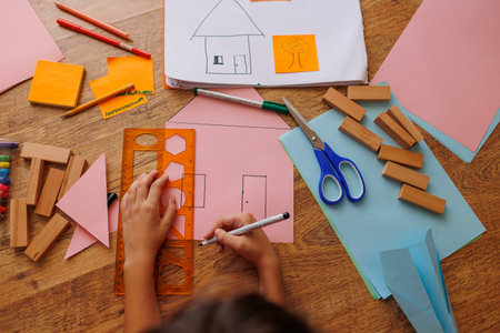 boy draws a house. the child makes a layout of the house. the boy is engaged with scissors and paper. the child is engaged in creativity at home. house layout.の写真素材