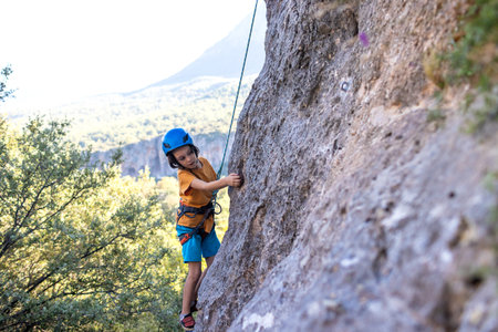 Children's rock climbing. The boy climbs a rock against the backdrop of mountains. extreme hobby. An athletic child trains to be strong. Climbing safety.の写真素材