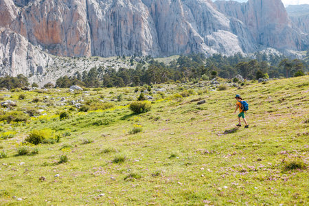 children's trip. child traveler with a backpack resting outdoors with rocky mountains in the background. Concept of summer vacation and hiking lifestyleの写真素材
