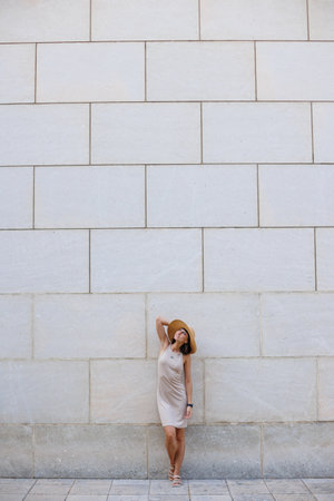 young girl posing near the wall. A girl in a beautiful dress and hat is having fun on the street standing near the wall. joy and pleasure.の写真素材