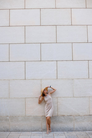 Young beautiful smiling girl in a trendy summer dress and hat posing near the wall on the street. Sexy carefree woman having fun outdoors.の写真素材