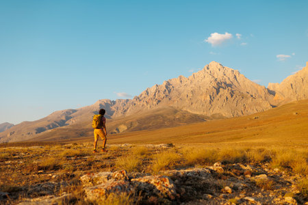 solo trip. a man with a backpack walks along the path against the backdrop of mountains. hiking in the mountains with a backpack. hiking and travel concept.の写真素材