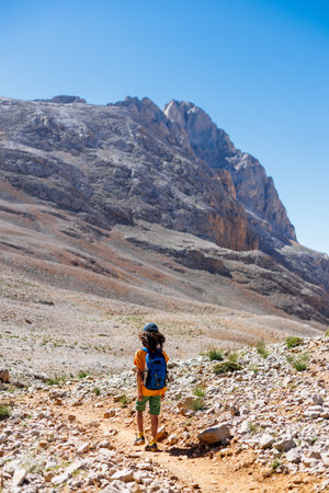 boy with a backpack walks along a mountain path. the child travels to the mountains with a backpack. mountain hike in high mountains. Turkey.の写真素材