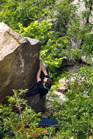 Bouldering on natural terrain, a strong man climbs a boulder, a man goes in for sports in nature, an effort to overcomeの写真素材