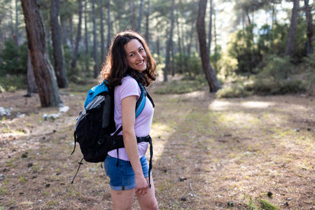 smiling girl walks through the forest with a backpack, hiking in the mountains on a sunny day.の写真素材
