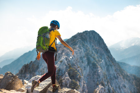 Woman climber with a backpack and a helmet in the mountains. A girl with a backpack walks along a mountain range. adventure and mountaineering concept. hiking with a backpack in the mountains.の写真素材