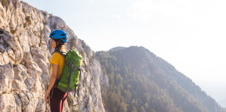 Woman climber with backpack and helmet enjoys amazing mountain view before climbing on a summer day. adventure and mountaineering concept.の写真素材