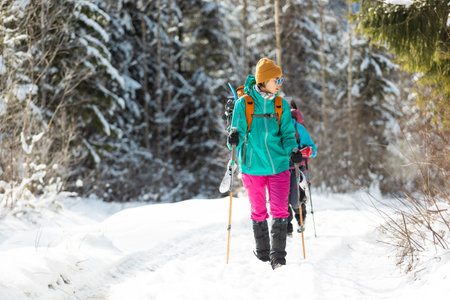 two girls with backpacks walk along a path in the winter mountains. hiking in the mountains. adventure in the mountains.の写真素材