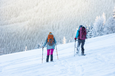 hiking in the mountains on snowshoes. two girls with backpacks go hiking in the snow. Travel and adventure concept. winter mountainsの写真素材