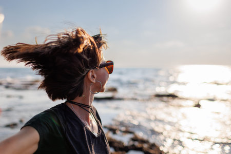portrait of a stylish girl in sunglasses with hair fluttering in the wind by the sea. Beautiful...