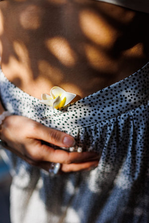 Female body in comfortable clothes with a flower. A model poses with a flower in her clothes. Health, motherhood and pregnancy concept.の写真素材