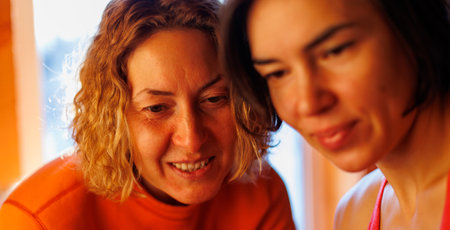 Two girlfriends look at a smartphone. two girls look through photos on a mobile phone, a woman shows her friend a photo on a smartphone.の写真素材
