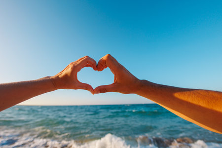 happy young couple showing heart shape with heart shaped hands on sea background, sign at sunrise over sea beach, ocean, outdoors, exotic coastline on summer day.の写真素材