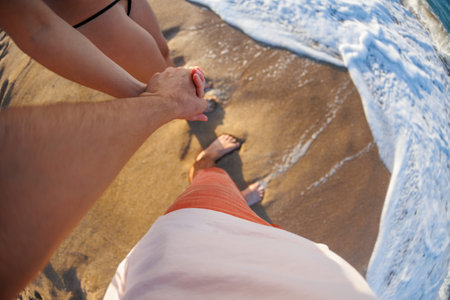 Romantic young couple holding hands on the beach, enjoying romance and love by the sea. Couple on summer vacation.の写真素材