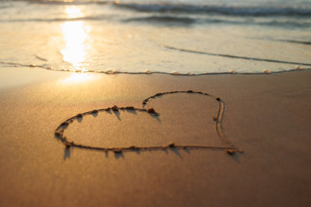 A heart is drawn on the sand on the beach at sunset. Romantic sunset on the beach. Heart shape. Heart symbol. Love.の写真素材