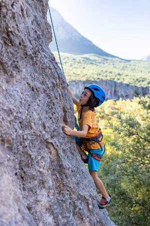 child rock climber. The boy climbs the rock. The child is engaged in rock climbing on natural terrain. Sports kid spends time actively. Do outdoor sports.の写真素材