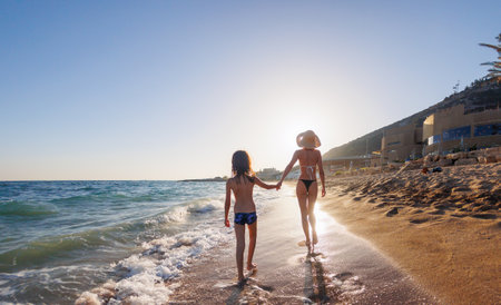 Happy young mother and her son are running along the sand on the sea beach, laughing and having fun together. young mother with a child. Family holiday at sea.の写真素材