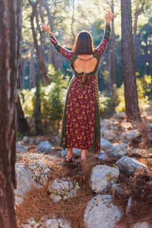 Young beautiful woman dancing in the forest with her hand raised. Concept of balance, harmony and health.の写真素材