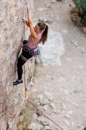 The girl climbs the rock. The climber is training to climb the rock. A strong athlete overcomes a difficult climbing route. Extreme hobby. A woman goes in for sports in nature. Natural rocky terrain.の写真素材