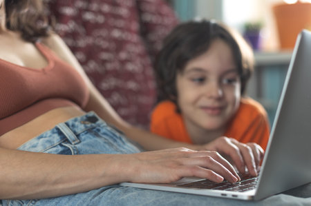 a woman with a child is sitting at a laptop, a boy spends time with his mother at homeの写真素材