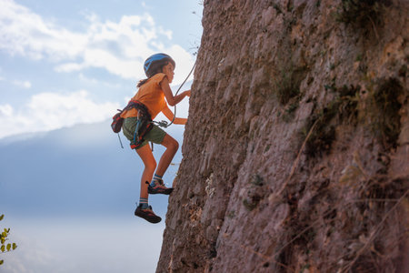 rock climber boy. child is practicing rock climbing. summer camp sport in nature. cute teenager climbing on a rock with belay, sport people lifestyle conceptの写真素材