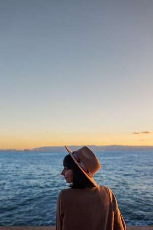girl looks at the sea. stylish and beautiful young woman in a coat and hat looks at the sea. Walk along the beach. calmness and tranquility.の写真素材