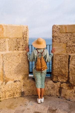 A stylish girl with a backpack stands on the street of the old city and looks at the sea. adventures and travel.の写真素材