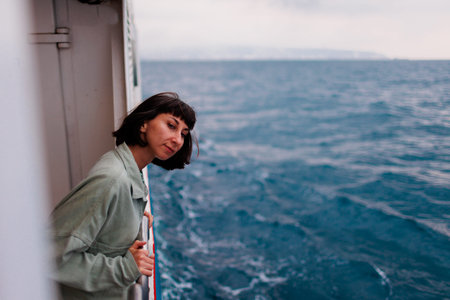 young woman stands on the deck of a cruise ship and looks at the setting sun, close-up silhouette. A...