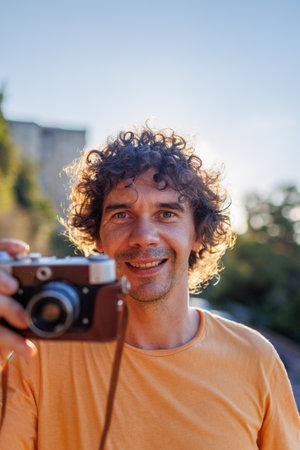 Portrait of a handsome stylish young man in a yellow T-shirt with a camera in his hands. film cameraの写真素材