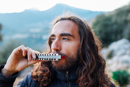 the musician enjoys playing the harmonica while standing on the street. a young man with long hair plays the harmonica.の写真素材